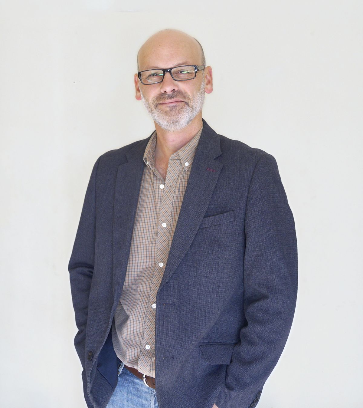 Jamie Tomlinson, in a navy jacket and checked shirt, standing against a plain wall